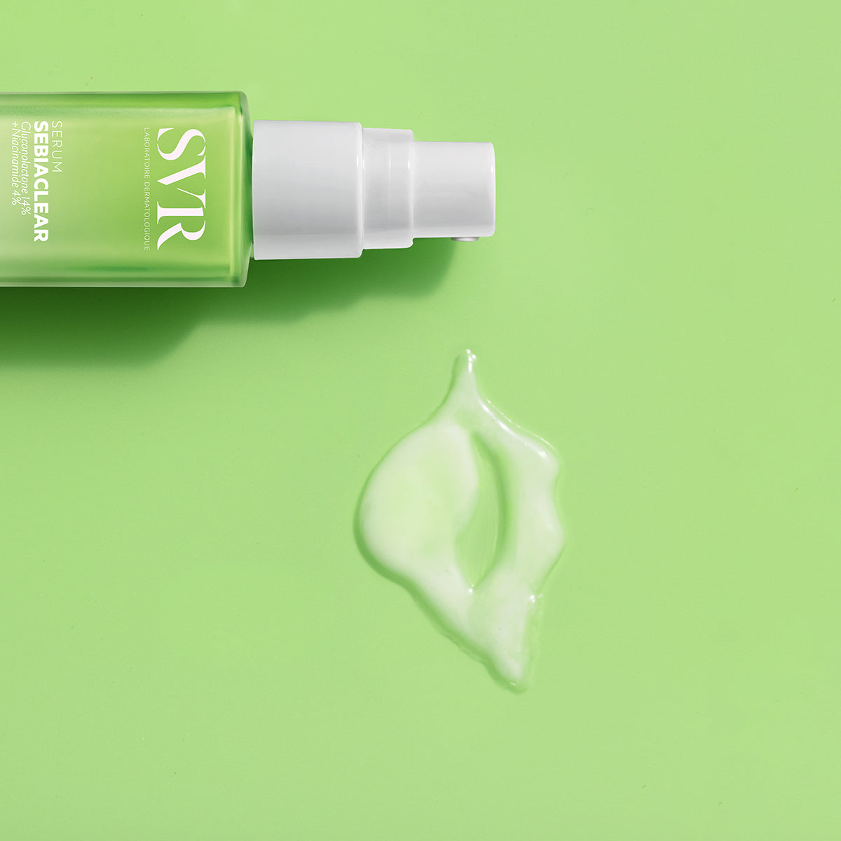 Frasco de SVR Sebiaclear Sérum con dosificador blanco sobre fondo verde claro y una gota de textura fluida al lado.