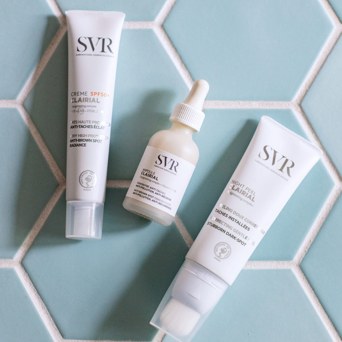 Tres productos SVR Clairial en envases blancos sobre un fondo de azulejos hexagonales de color azul claro.