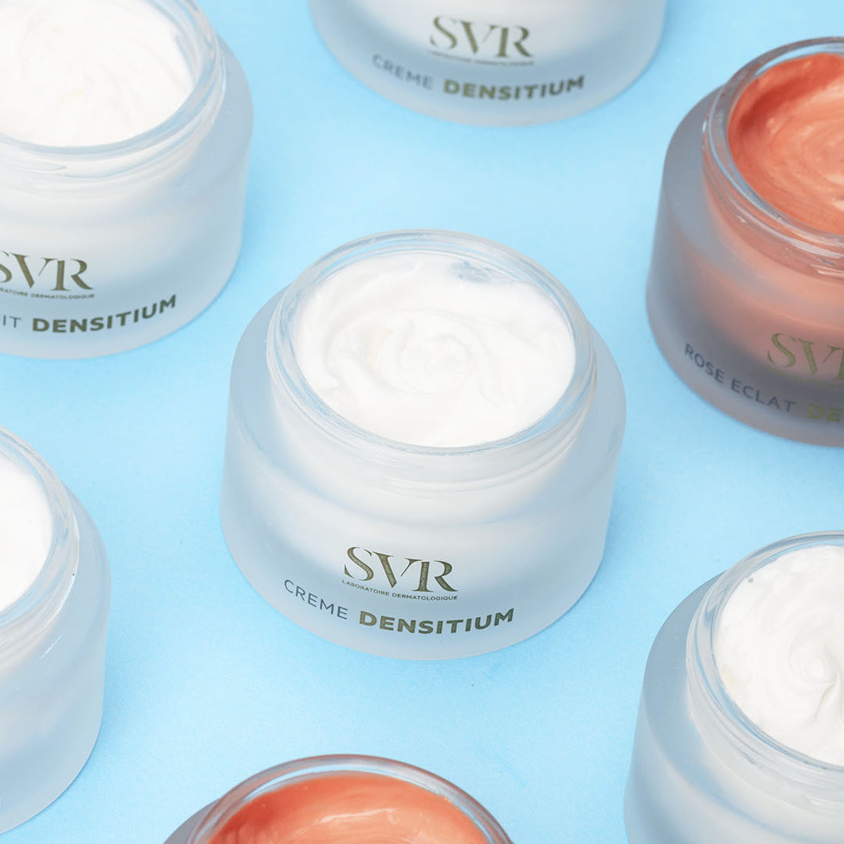 Open jars of SVR Densitium cream with white and rose-tinted textures arranged on a light blue background.