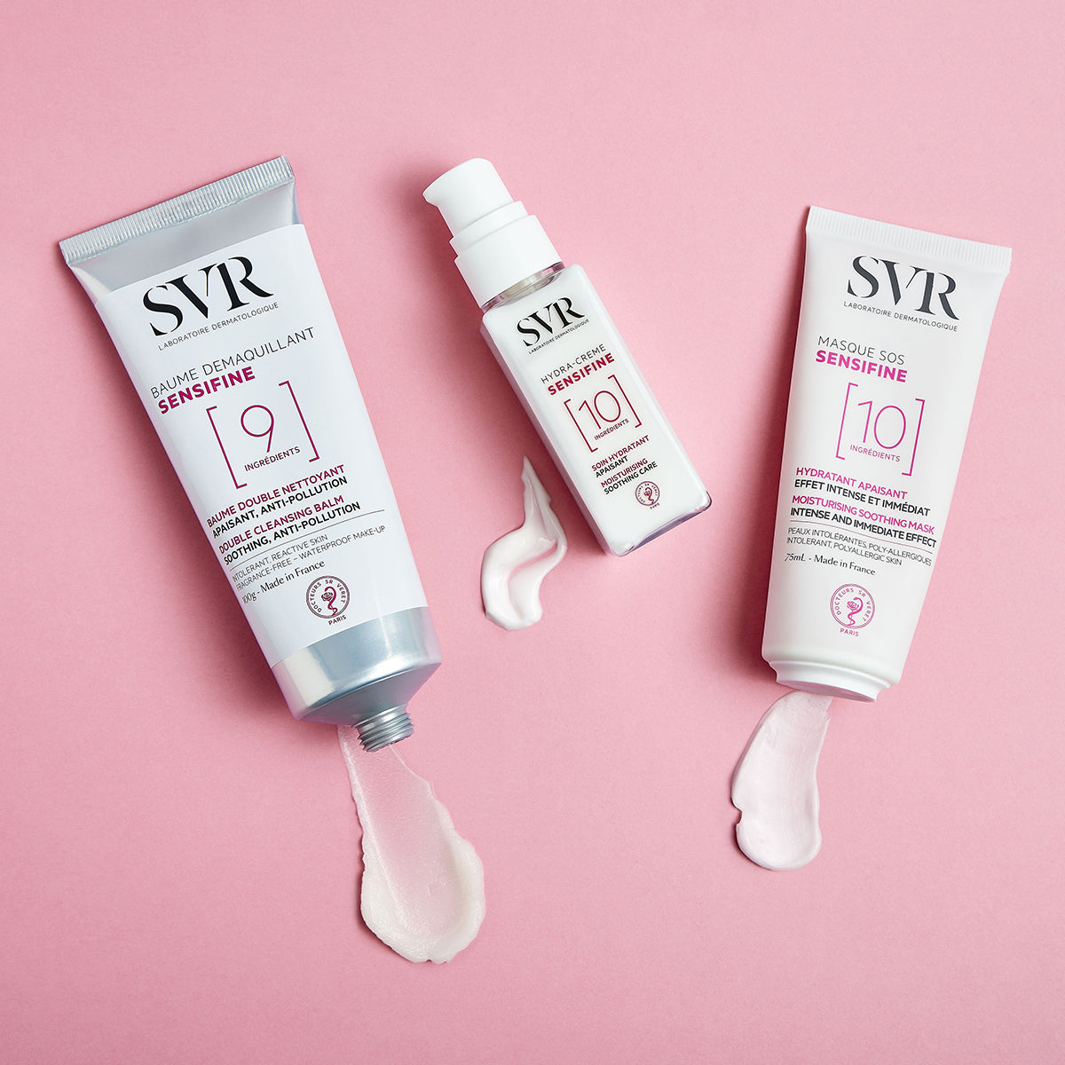 Tres productos SVR Sensifine en envases blancos con detalles rosas sobre fondo rosa, mostrando texturas de crema y bálsamo.