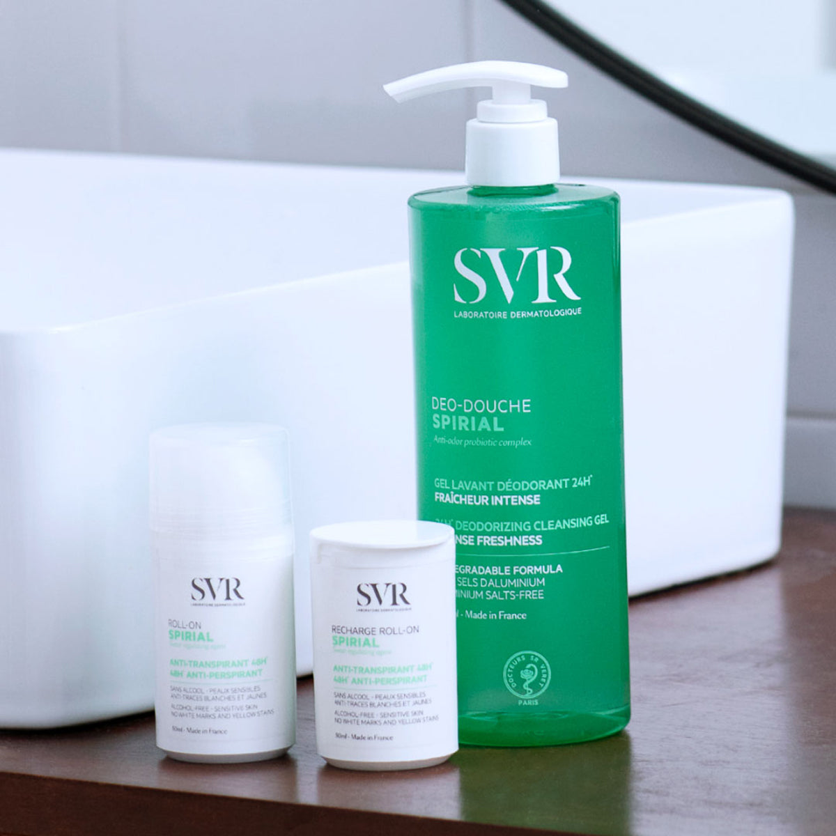Gel de ducha desodorante SVR Spirial verde con dos desodorantes roll-on blancos sobre una superficie de madera.