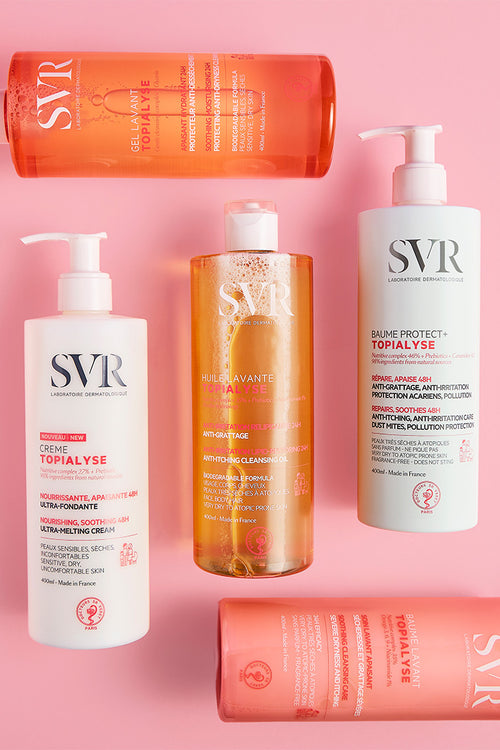 Cinco botellas de SVR Topialyse con dosificador sobre fondo rosa, incluyendo geles, aceites y bálsamos reparadores de 400ml.