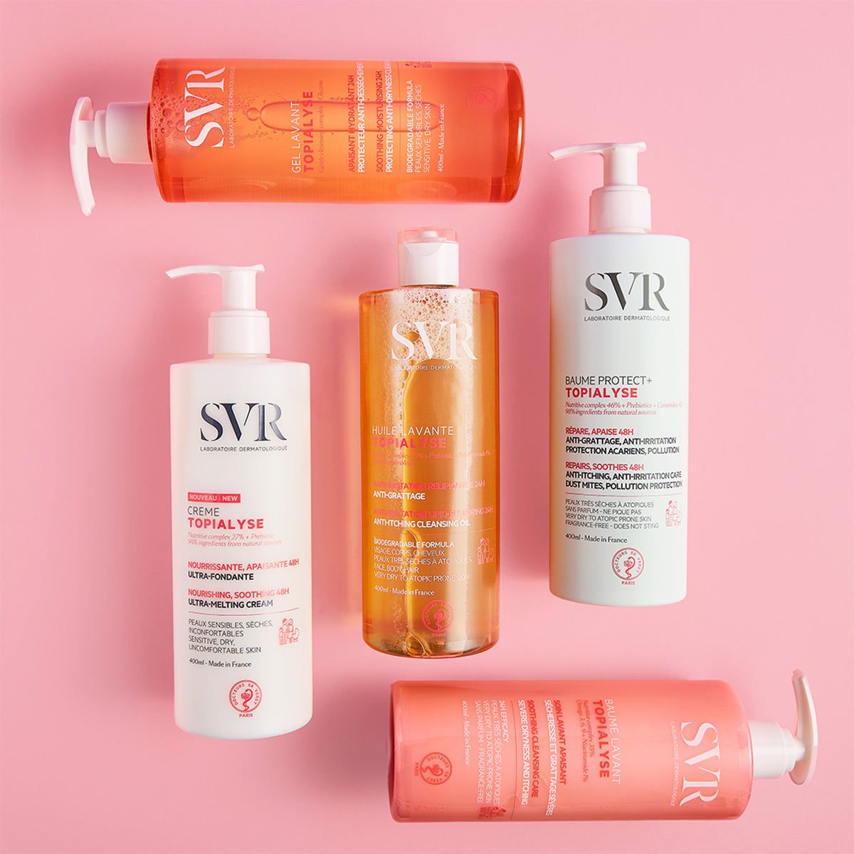 Cinco envases de 400ml de SVR Topialyse con dosificadores sobre un fondo rosa, incluyendo aceites y cremas para pieles sensibles.