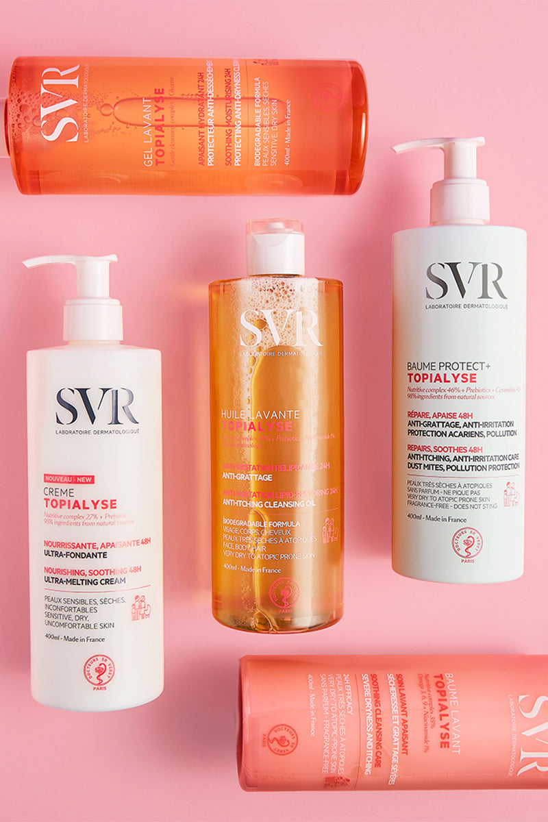 Cinco envases de SVR Topialyse con dosificador sobre fondo rosa, incluyendo cremas, aceites y geles limpiadores dermatológicos.