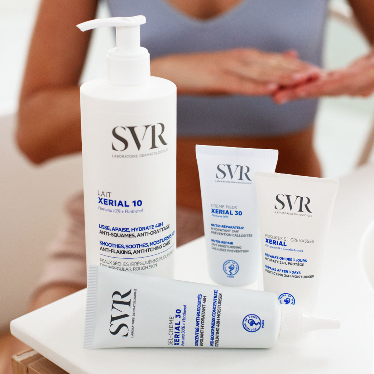 Envase dosificador y tubos de crema SVR Xerial para el cuidado reparador de pies secos y agrietados sobre mesa blanca.