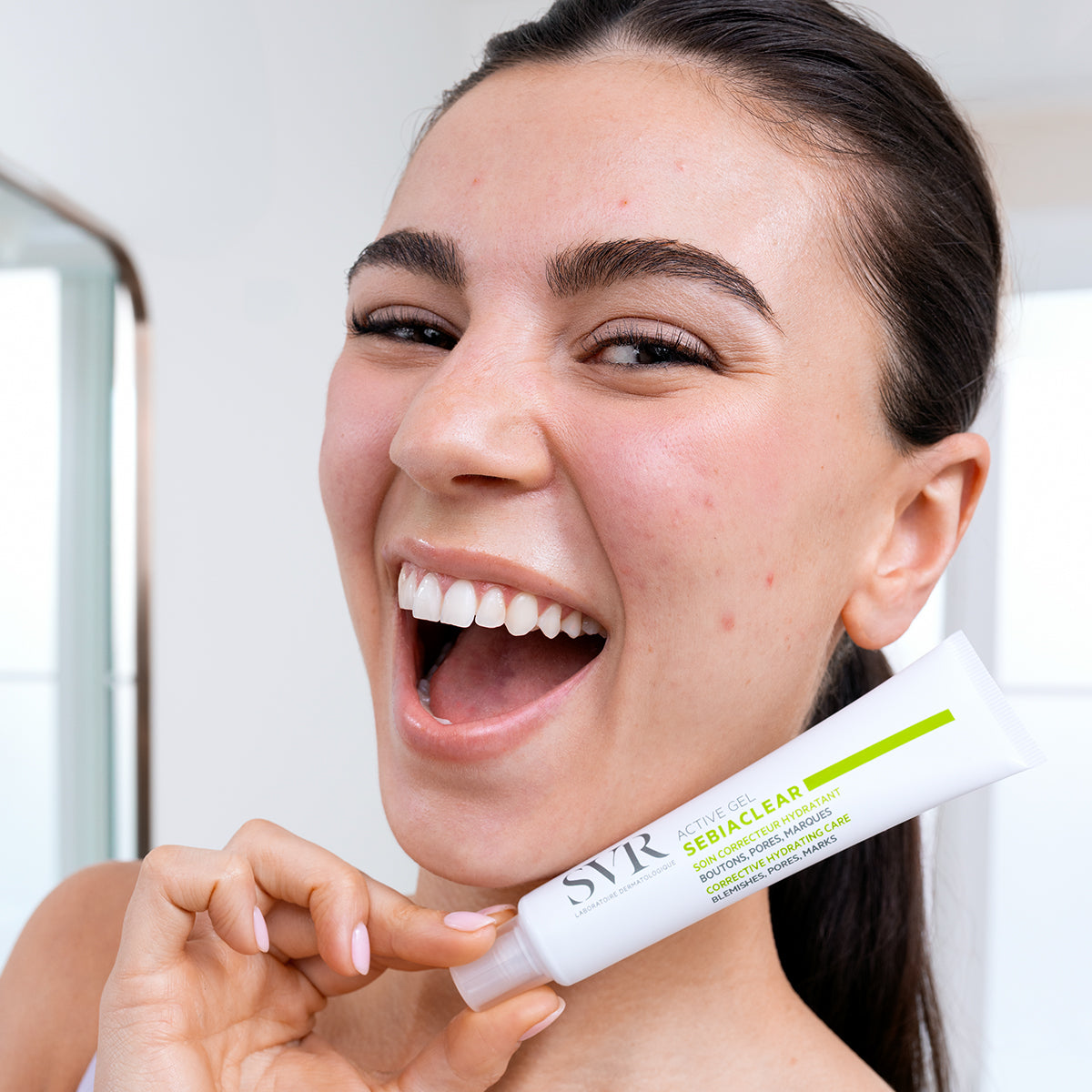 Mujer sonriente sosteniendo un tubo blanco de SVR Sebiaclear Active Gel con detalles en verde brillante.