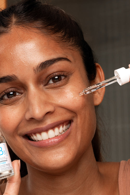 Mujer sonriente aplicando SVR B3 Ampoule Hydra con gotero sobre su rostro para hidratar y reparar la piel sensible.
