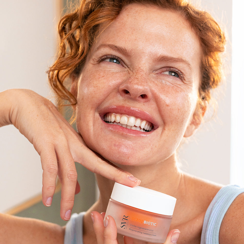Mujer pelirroja con pecas y piel luminosa sonriendo, mostrando el glow recuperado gracias a un tratamiento facial con vitamina C de SVR.
