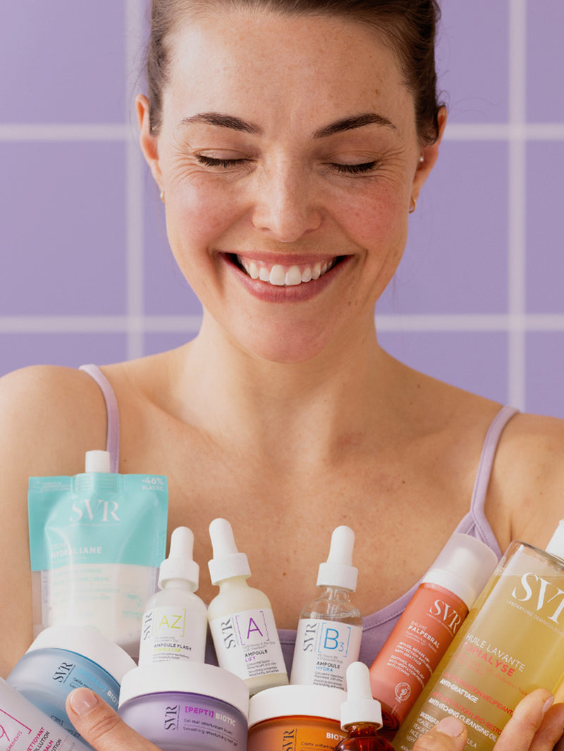 Mujer sonriendo con productos dermocosméticos de SVR en las manos, ilustrando una rutina de cuidado de la piel.