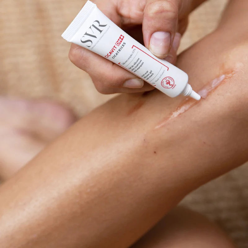 Tubo blanco de gel SVR Cicavit DM+ aplicándose sobre una cicatriz en la piel para su tratamiento dermatológico.