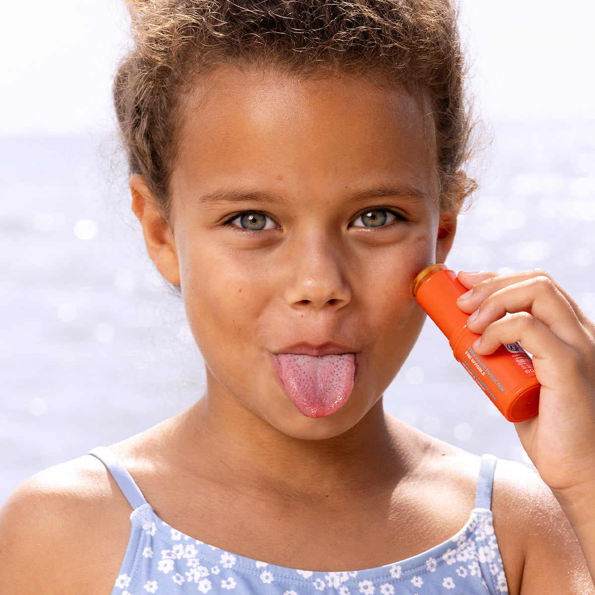 Niña aplicando protector solar SUN SECURE Easy Stick SPF50+ en su mejilla con un envase naranja brillante.