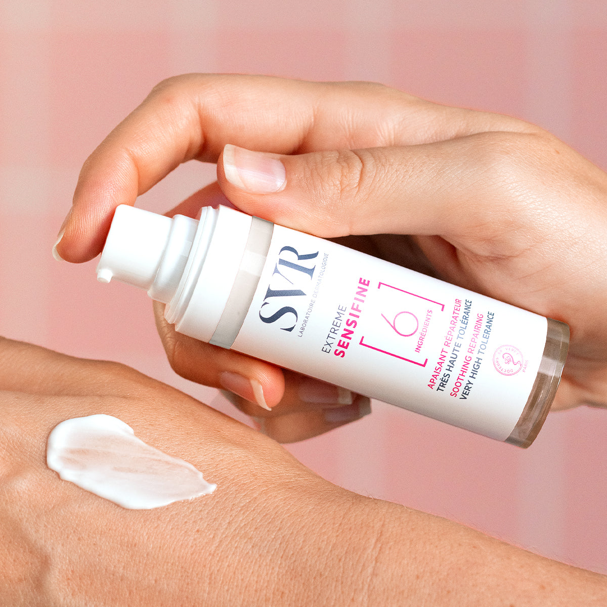 Frasco dosificador blanco de SVR Sensifine Extrême con crema reparadora aplicada sobre el dorso de una mano.