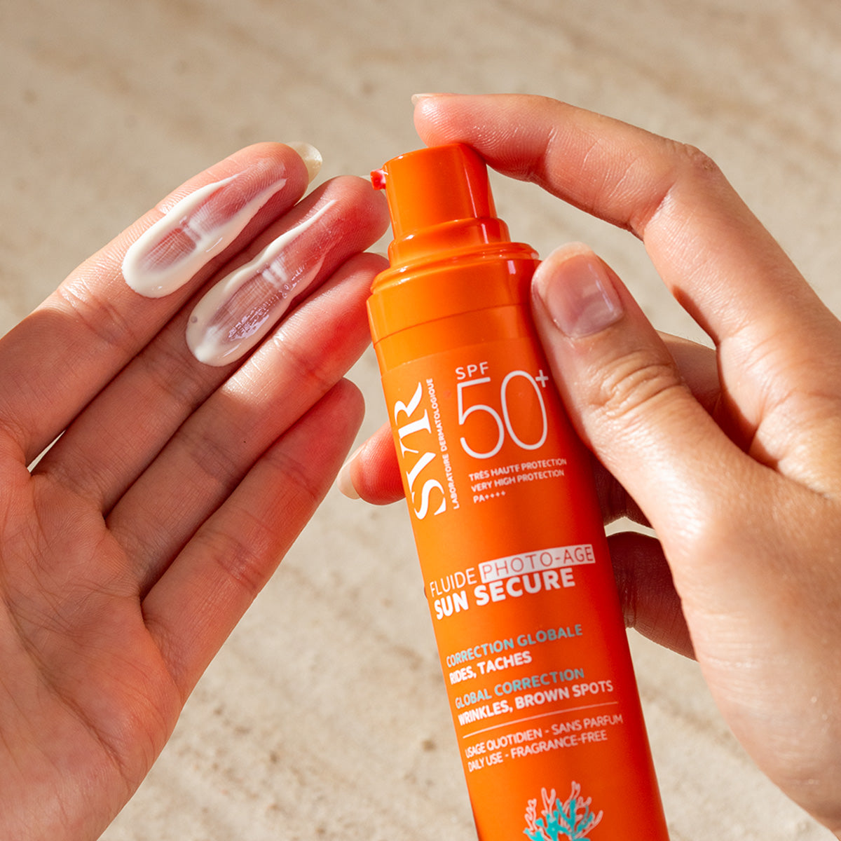 Hands holding an orange SVR SUN SECURE SPF50+ pump bottle with white sunscreen cream dispensed on the palm.