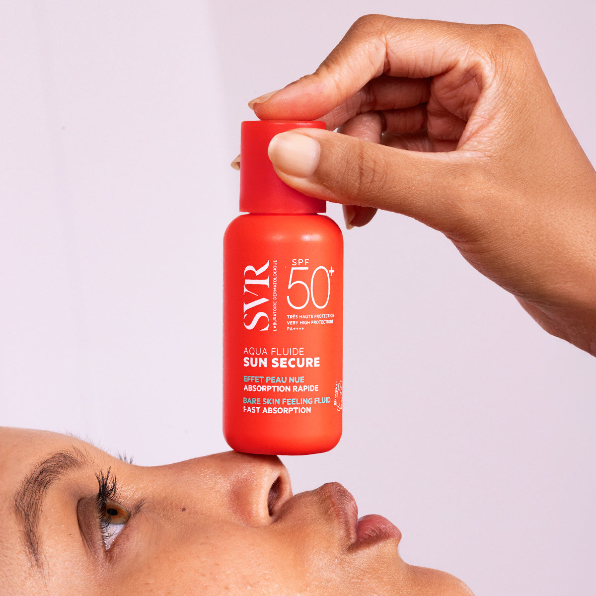 Frasco naranja de protector solar SVR Sun Secure SPF50+ sostenido sobre la nariz de una persona.